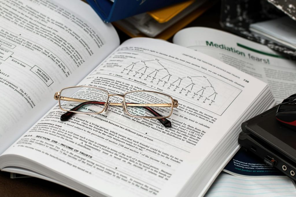 An open book with reading glasses, surrounded by study materials and a laptop, ideal for education themes.